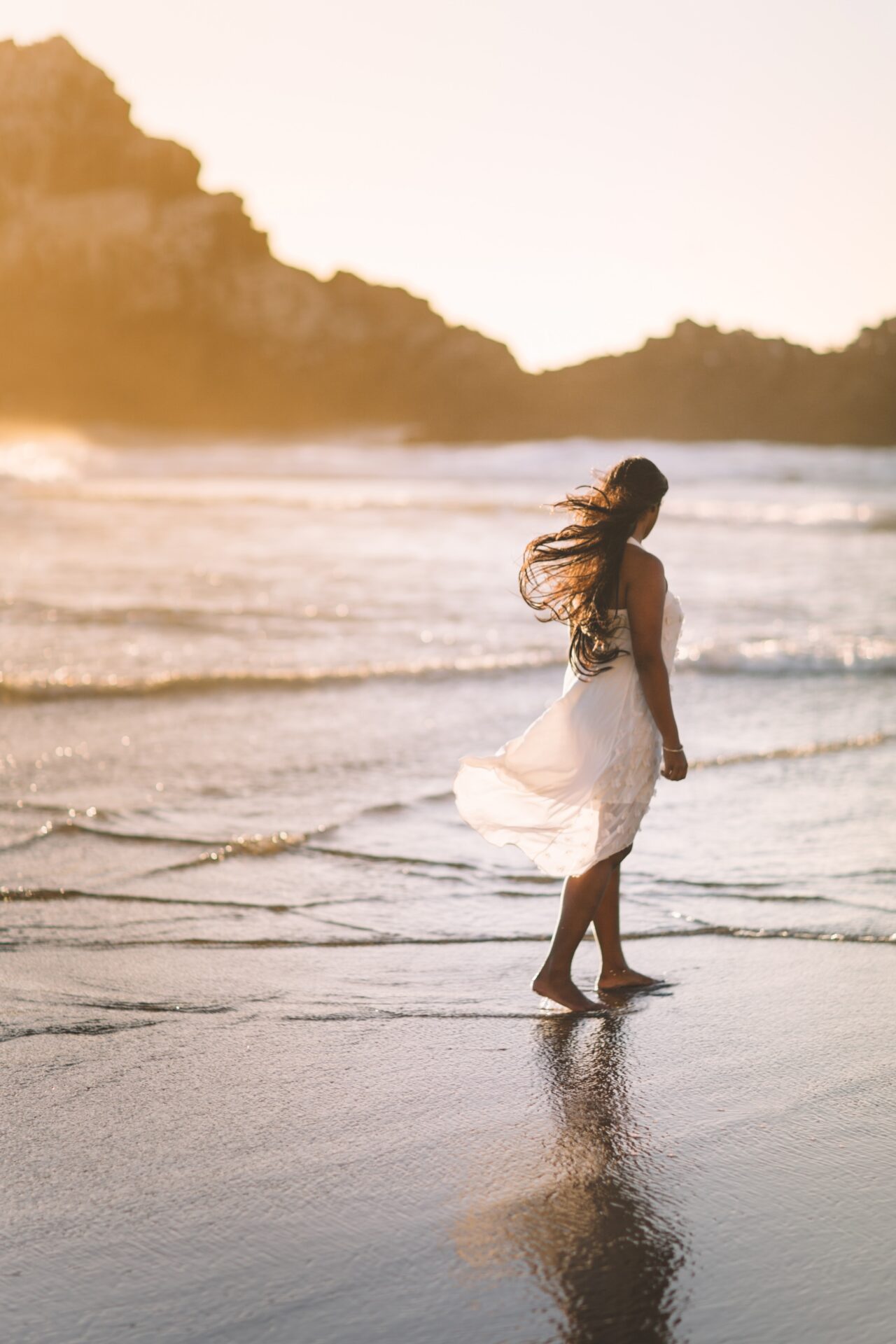 woman walking barefoot on the beach with sunlight in the background